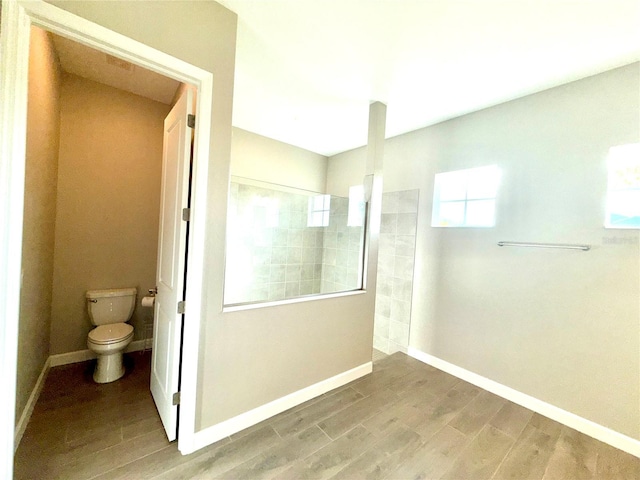 bathroom featuring wood finish floors, baseboards, toilet, and walk in shower