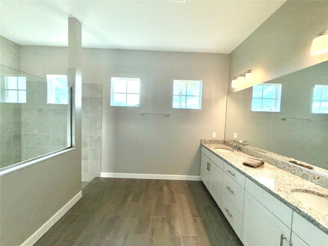 bathroom featuring wood finished floors, walk in shower, a sink, and baseboards