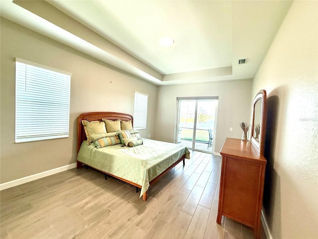 bedroom with access to exterior, a raised ceiling, visible vents, light wood-style floors, and baseboards