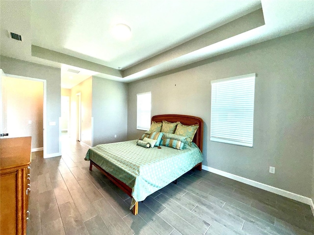 bedroom with a tray ceiling, wood finish floors, and baseboards