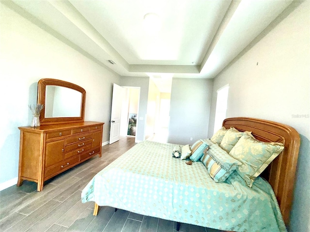 bedroom featuring visible vents, a tray ceiling, baseboards, and wood finish floors