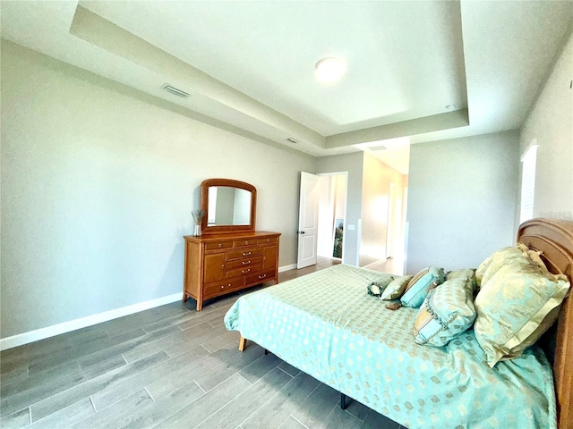 bedroom with a tray ceiling, wood finish floors, visible vents, and baseboards