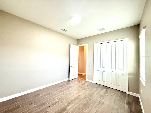 unfurnished bedroom with a closet, visible vents, baseboards, and wood finished floors