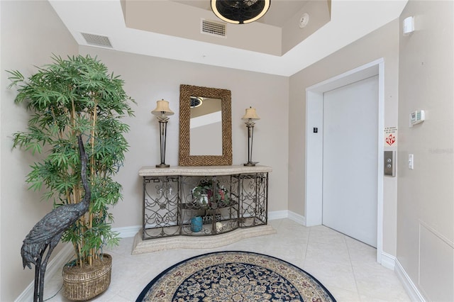 hallway with visible vents, baseboards, tile patterned floors, a tray ceiling, and elevator