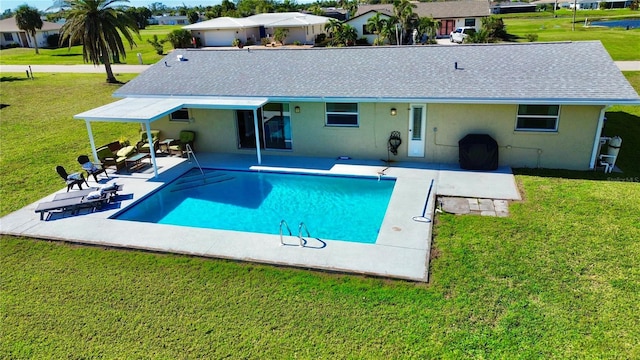 back of property with a shingled roof, a lawn, stucco siding, an outdoor pool, and a patio area