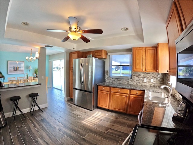 kitchen with a sink, appliances with stainless steel finishes, backsplash, brown cabinets, and a raised ceiling