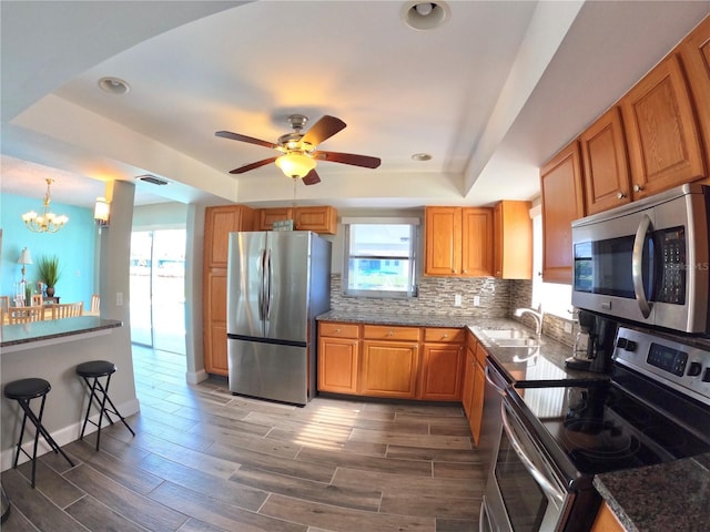 kitchen featuring dark wood-type flooring, a sink, appliances with stainless steel finishes, backsplash, and a raised ceiling