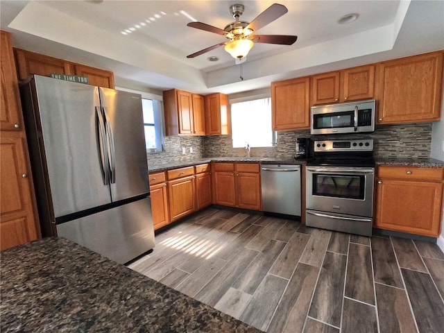 kitchen with appliances with stainless steel finishes, wood tiled floor, a raised ceiling, and decorative backsplash