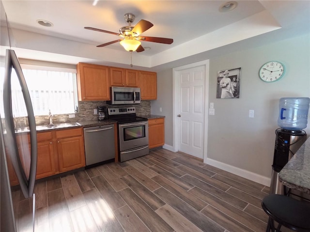 kitchen with decorative backsplash, appliances with stainless steel finishes, wood tiled floor, a sink, and baseboards