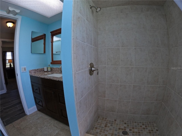 bathroom with tile patterned flooring, a tile shower, and vanity