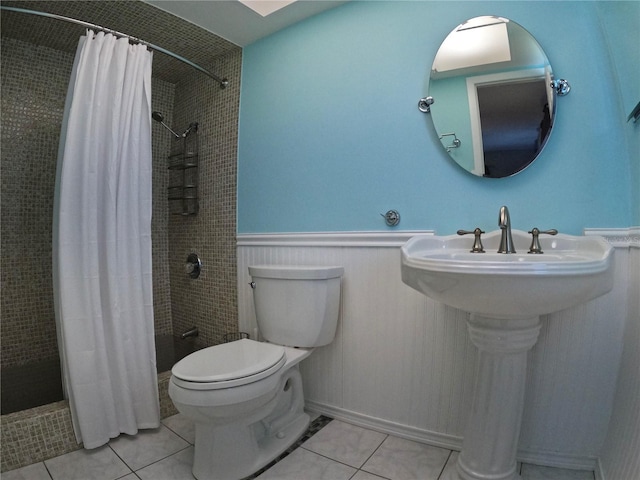 bathroom featuring a tile shower, wainscoting, tile patterned flooring, and toilet