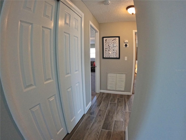 corridor featuring baseboards, wood tiled floor, visible vents, and a textured ceiling