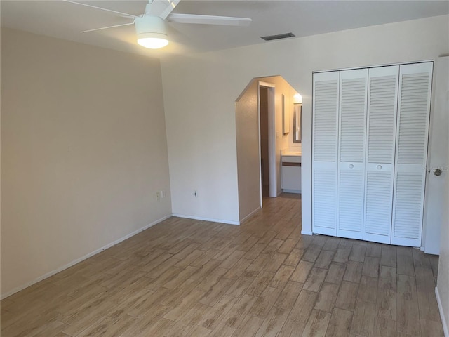 unfurnished bedroom with visible vents, arched walkways, ceiling fan, wood finished floors, and a closet