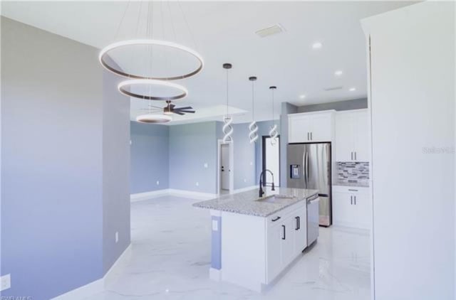 kitchen featuring marble finish floor, stainless steel appliances, backsplash, white cabinetry, and a sink