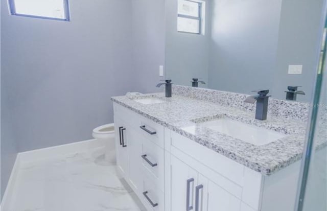 full bathroom featuring toilet, marble finish floor, double vanity, and a sink