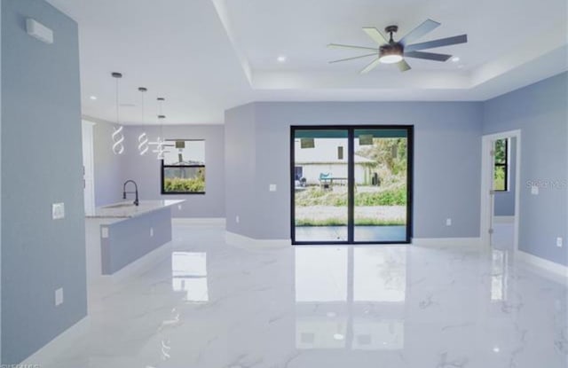 empty room featuring a healthy amount of sunlight, marble finish floor, and a tray ceiling