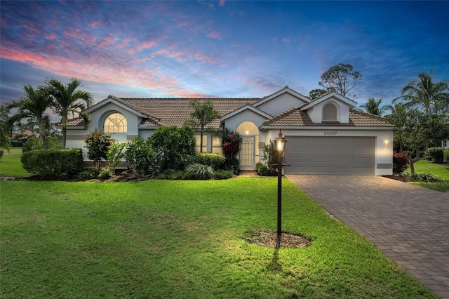 view of front of home with a tile roof, an attached garage, decorative driveway, a front yard, and stucco siding