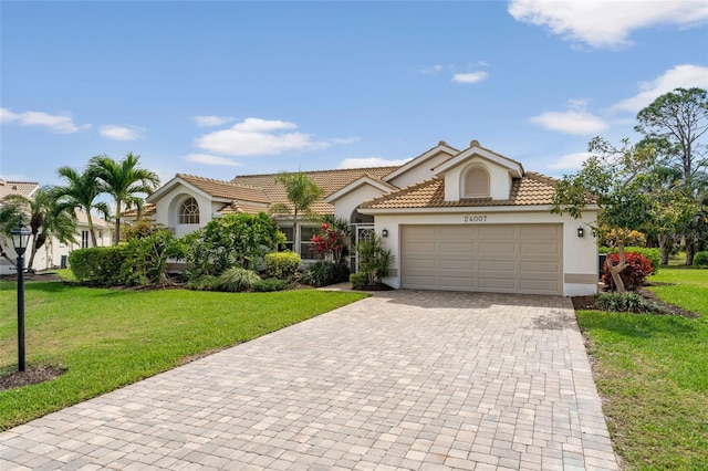 view of front of home featuring an attached garage, a tiled roof, decorative driveway, stucco siding, and a front lawn