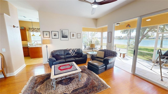 living area with ceiling fan, light wood-type flooring, a water view, and baseboards