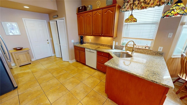 kitchen with light tile patterned floors, light stone counters, a peninsula, white dishwasher, and a sink