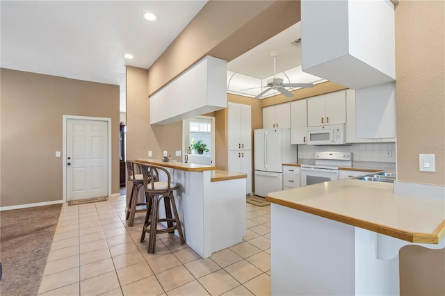 kitchen with a peninsula, white appliances, a ceiling fan, tasteful backsplash, and a kitchen bar