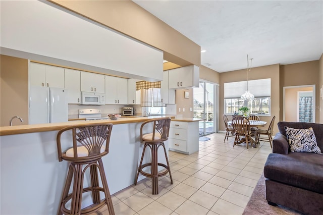 kitchen featuring white appliances, light tile patterned floors, a kitchen breakfast bar, open floor plan, and white cabinetry