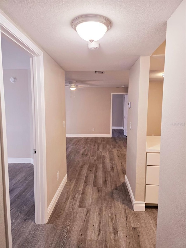 hallway with visible vents, a textured ceiling, baseboards, and wood finished floors