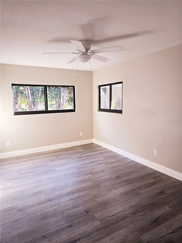 empty room with dark wood-style floors, a ceiling fan, and baseboards