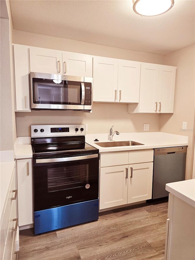 kitchen with stainless steel appliances, light wood-type flooring, a sink, and white cabinets