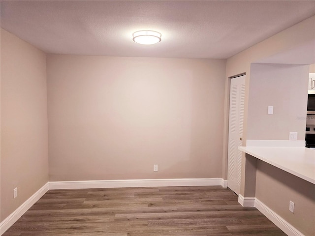 unfurnished dining area featuring dark wood-style floors, a textured ceiling, and baseboards