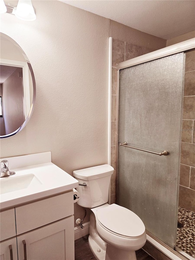 bathroom featuring a stall shower, a textured wall, toilet, wood finished floors, and vanity