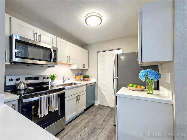 kitchen with a sink, light countertops, stainless steel appliances, white cabinetry, and wood finished floors