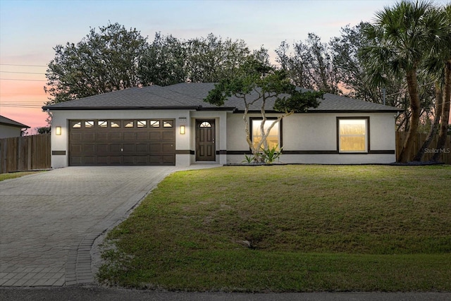 view of front facade featuring decorative driveway, stucco siding, an attached garage, fence, and a front lawn