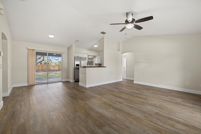 unfurnished living room with arched walkways, dark wood finished floors, a ceiling fan, vaulted ceiling, and baseboards