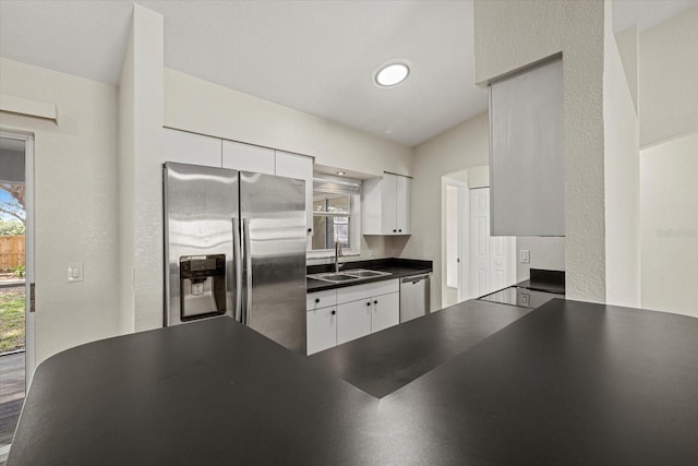 kitchen with a textured wall, a sink, white cabinetry, appliances with stainless steel finishes, and dark countertops