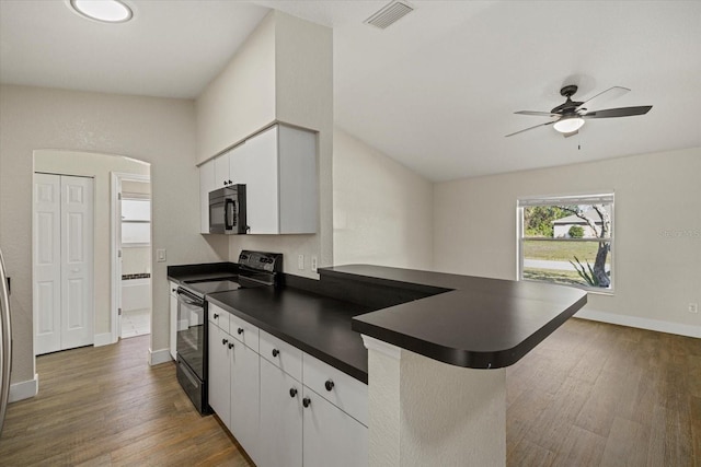 kitchen with a peninsula, dark wood-type flooring, visible vents, black appliances, and dark countertops