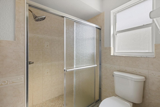 full bathroom with tile walls, a shower stall, and toilet