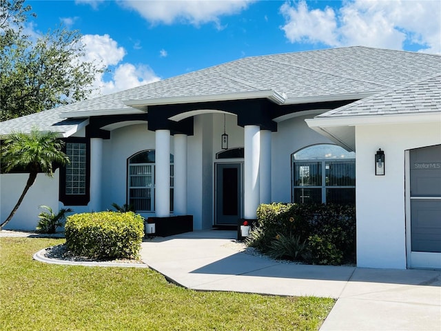 view of exterior entry featuring roof with shingles, a yard, and stucco siding