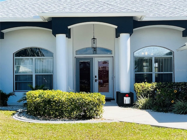 view of exterior entry with roof with shingles and stucco siding