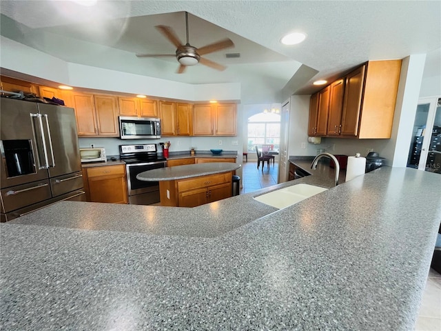 kitchen featuring brown cabinetry, a ceiling fan, appliances with stainless steel finishes, a peninsula, and a sink