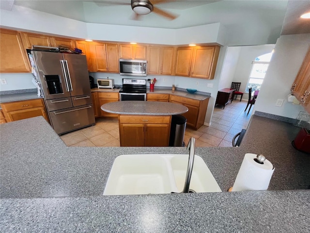 kitchen with light tile patterned floors, stainless steel appliances, a ceiling fan, and a center island