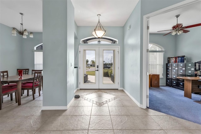 carpeted foyer featuring ceiling fan with notable chandelier, baseboards, and french doors