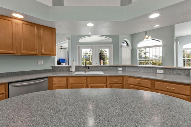 kitchen featuring recessed lighting, dark countertops, stainless steel dishwasher, brown cabinetry, and a sink