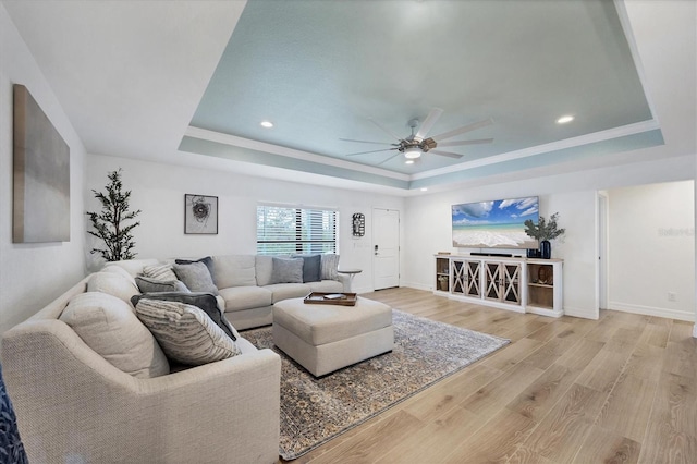 living area with baseboards, ceiling fan, a tray ceiling, and light wood-style floors