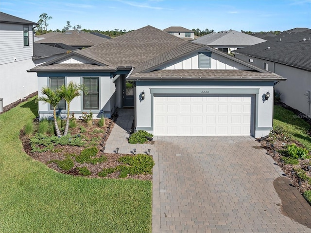 ranch-style home with roof with shingles, an attached garage, decorative driveway, a front lawn, and stucco siding