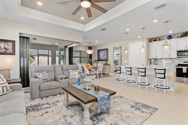 living area featuring light tile patterned floors, a tray ceiling, ornamental molding, and visible vents