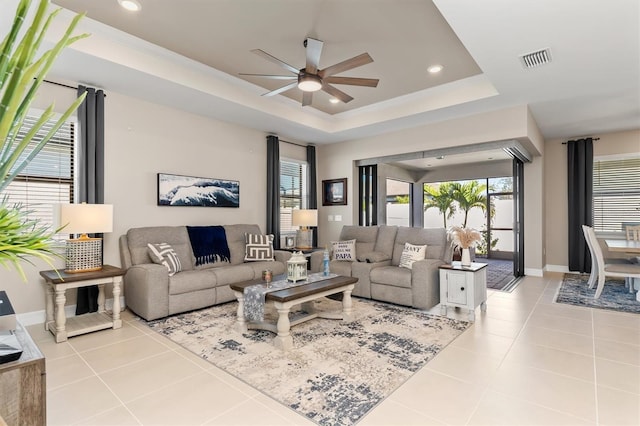 living area with visible vents, a raised ceiling, a wealth of natural light, and tile patterned floors