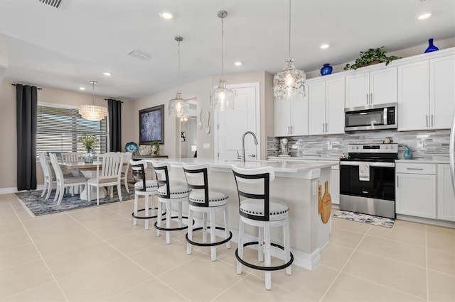 kitchen with light tile patterned floors, a center island with sink, stainless steel appliances, light countertops, and a kitchen bar