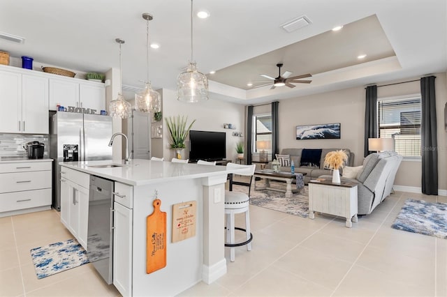 kitchen with a tray ceiling, light tile patterned floors, a healthy amount of sunlight, a sink, and dishwasher