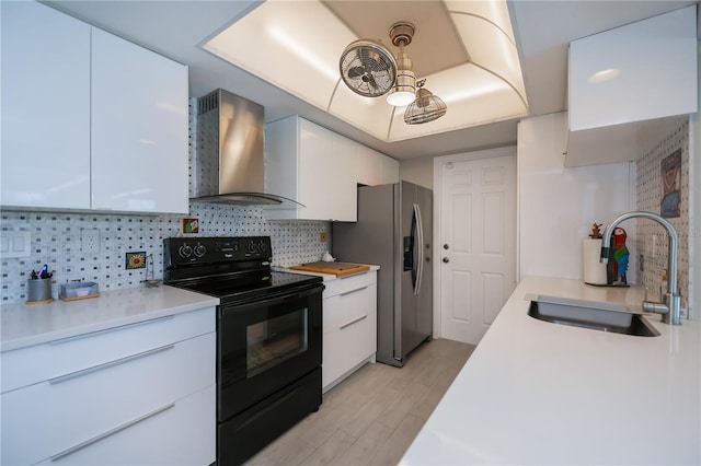 kitchen with stainless steel refrigerator with ice dispenser, a raised ceiling, black range with electric stovetop, a sink, and wall chimney range hood